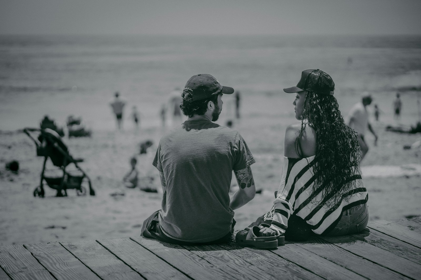 a man and a woman sitting on a pier looking at the beach